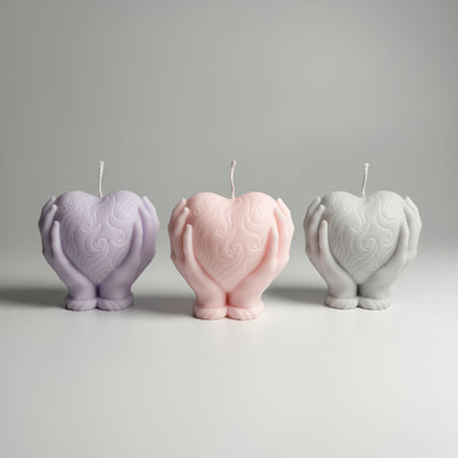 Bougie parfumée artisanale forme coeur dans les mains en rose, violet et gris